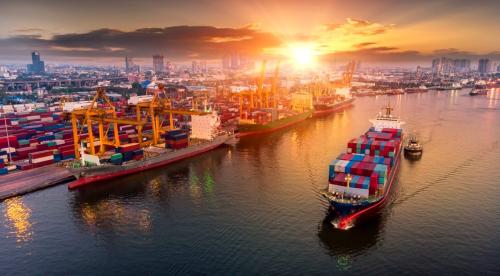 Container cargo ship sailing in front of shipyard